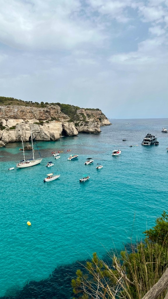 Turquoise cove of Cala Macarella, Menorca, with sailboats and limestone cliffs