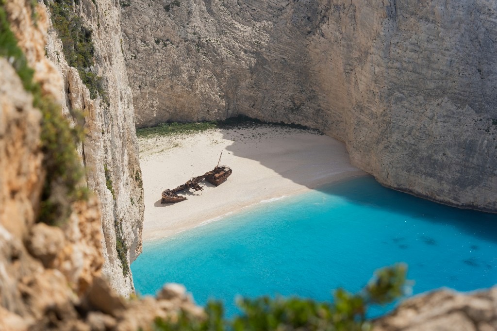 Close-up of rusted shipwreck on white sand at Navagio Beach, framed by limestone cliffs