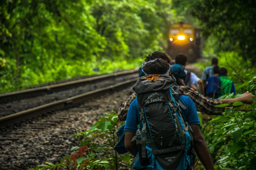 Group of backpackers with large rucksacks walking alongside a jungle railway track with a train approaching