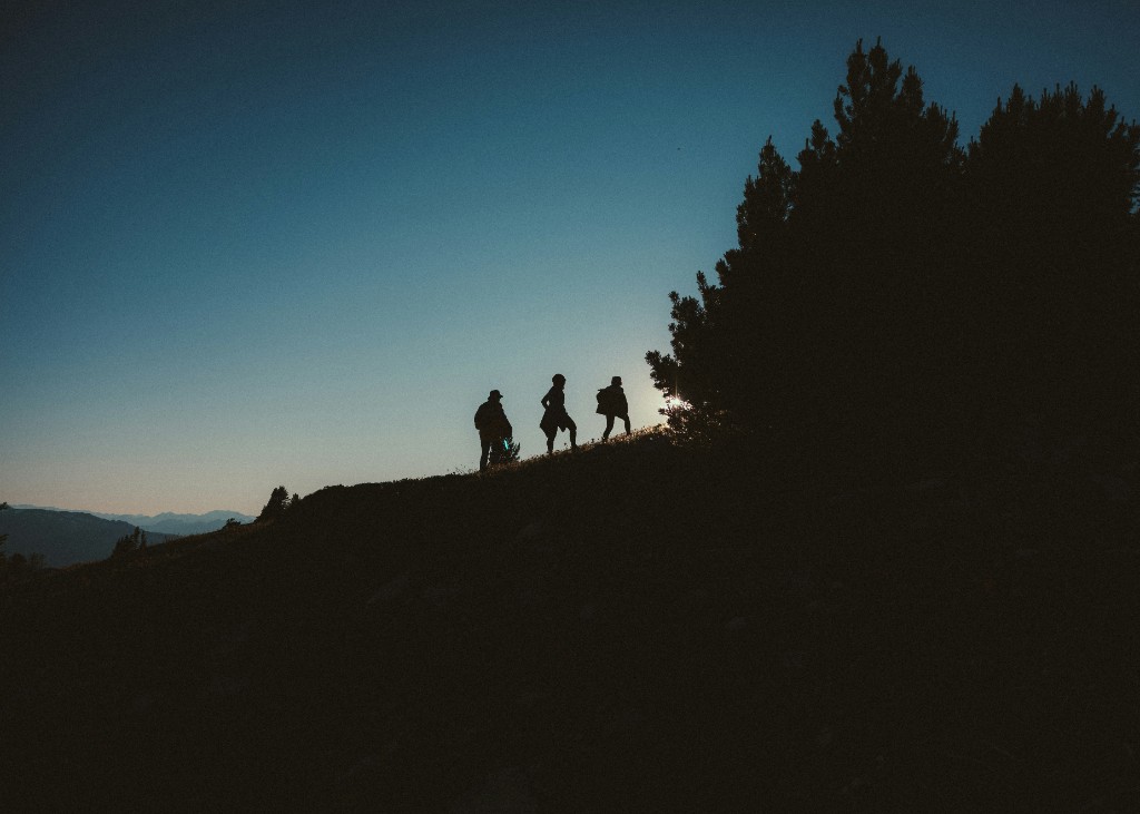 Silhouette of three friends hiking together on a hill at dusk with mountains in the background
